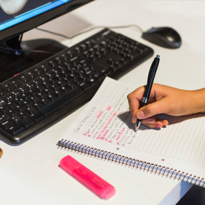 crop-hand-writing-notebook-near-computer